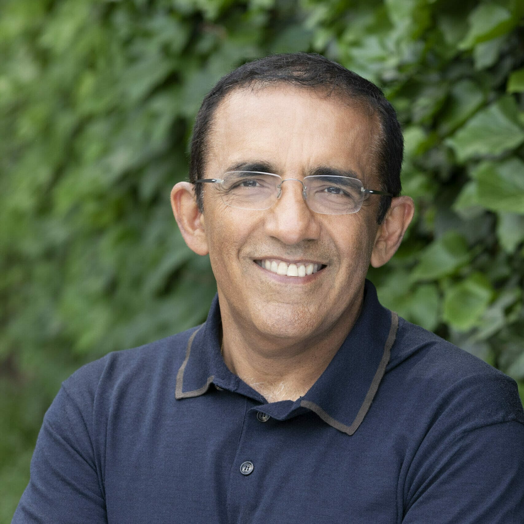 Headshot of Ranjay Gulati in a dark blue shirt against a leafy green background